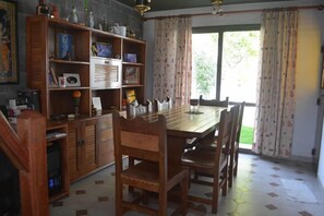 A dining area with a wooden table and chairs, a bookshelf with various items, and a window with curtains.