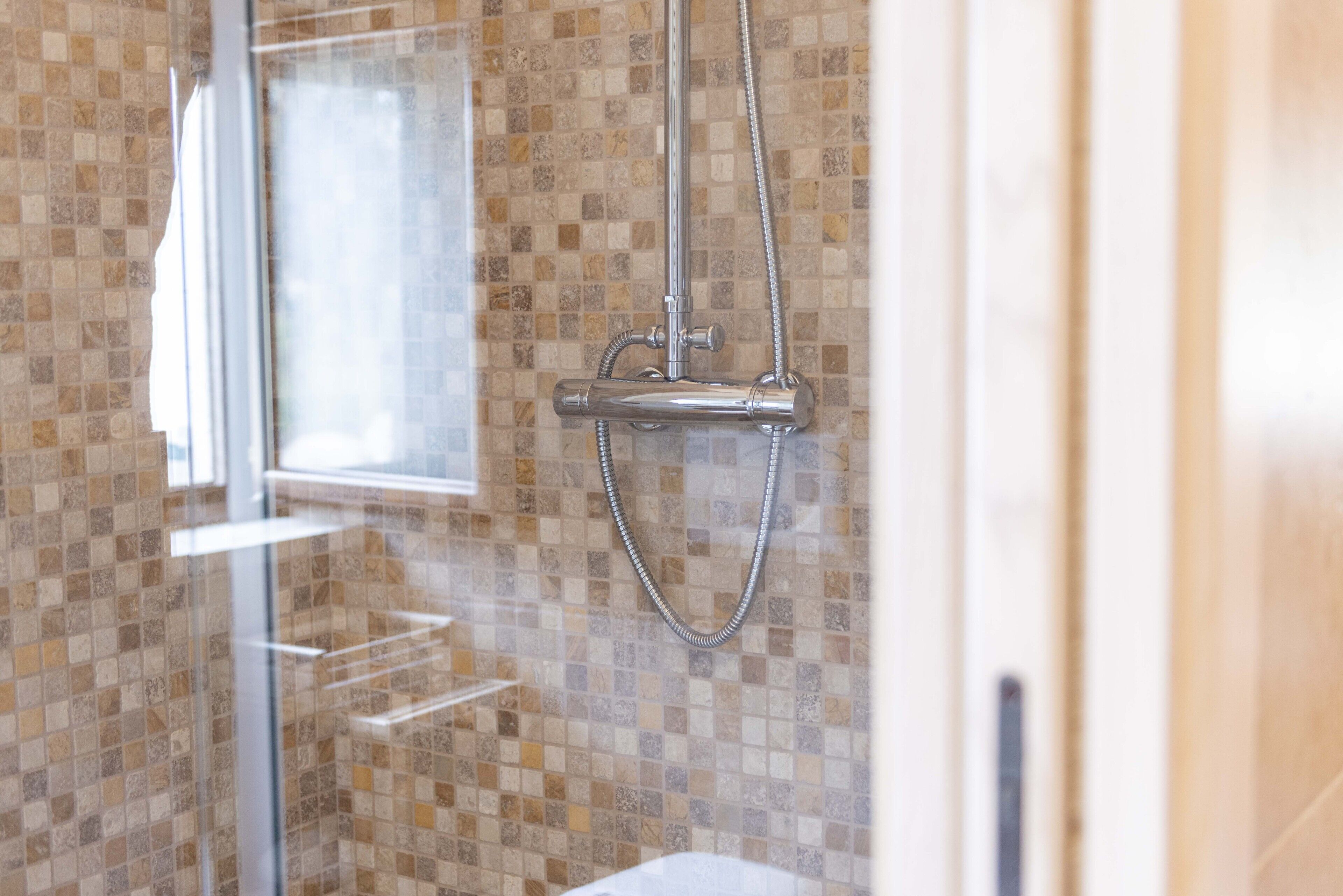 A shower with a glass door, a tiled wall, and a window.