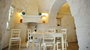 A rustic stone interior with a dining table and chairs, a wine bottle, and a candle holder.