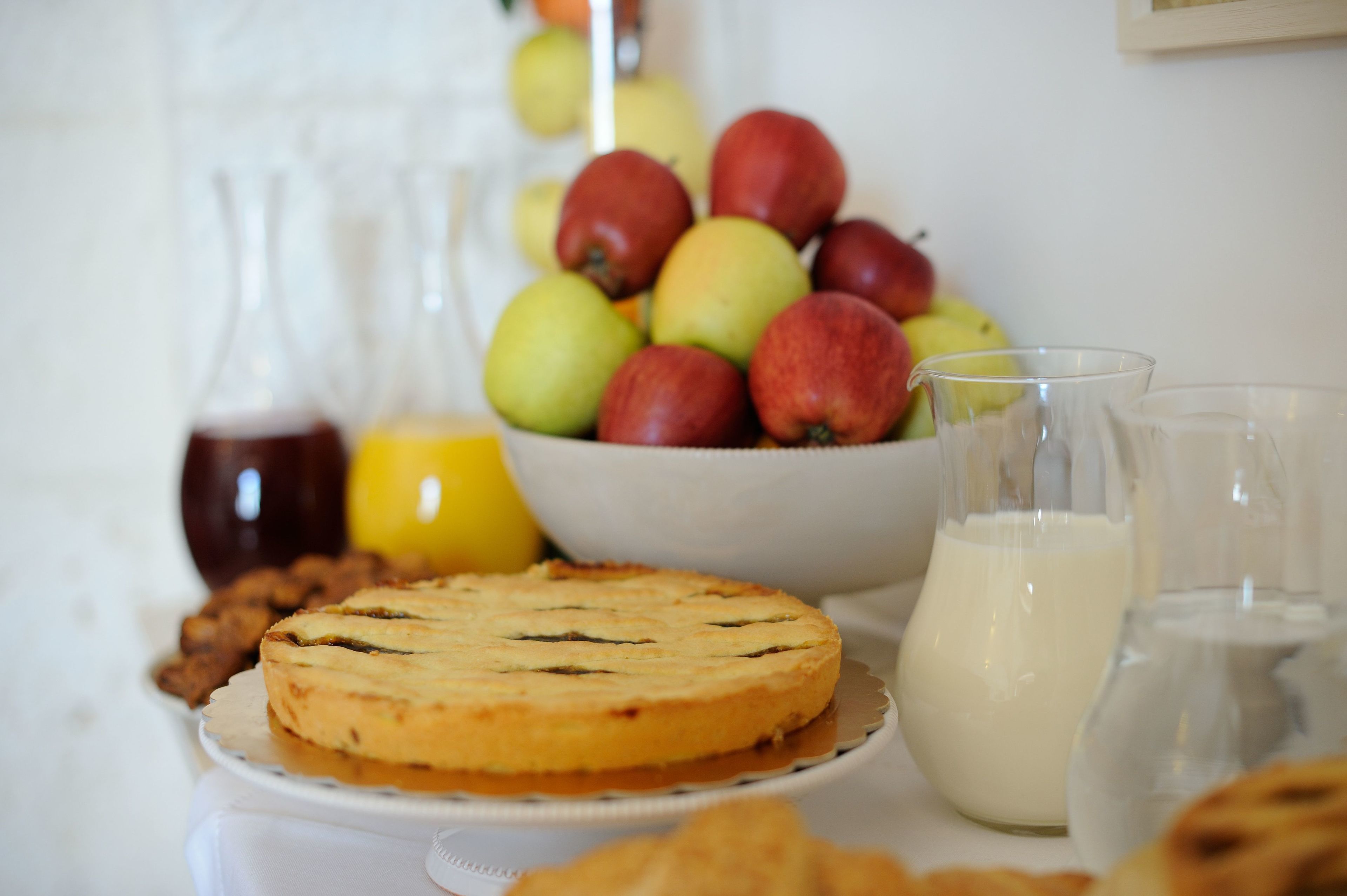 A table with a pie, a bowl of fruit, and two glasses of milk.