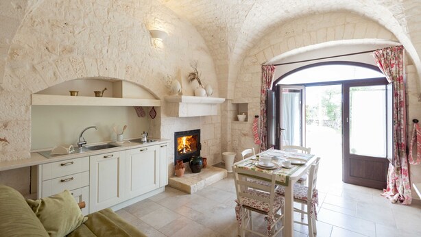 A cozy kitchen with a stone wall, a fireplace, and a dining area with a table and chairs.
