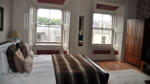 A bedroom with a large bed, two windows, a wardrobe, and a lamp. - The Bank Guest House (Hawick)
