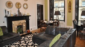 A living room with a fireplace, leather sofas, a patterned rug, and a dining area with a table and chairs. - The Bank Guest House (Hawick)