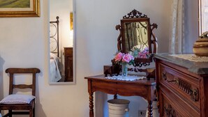 Ein Zimmer mit einem Holzstuhl, einem Holzschrank, einem Spiegel und einem kleinen Tisch mit einer Blumenvase.