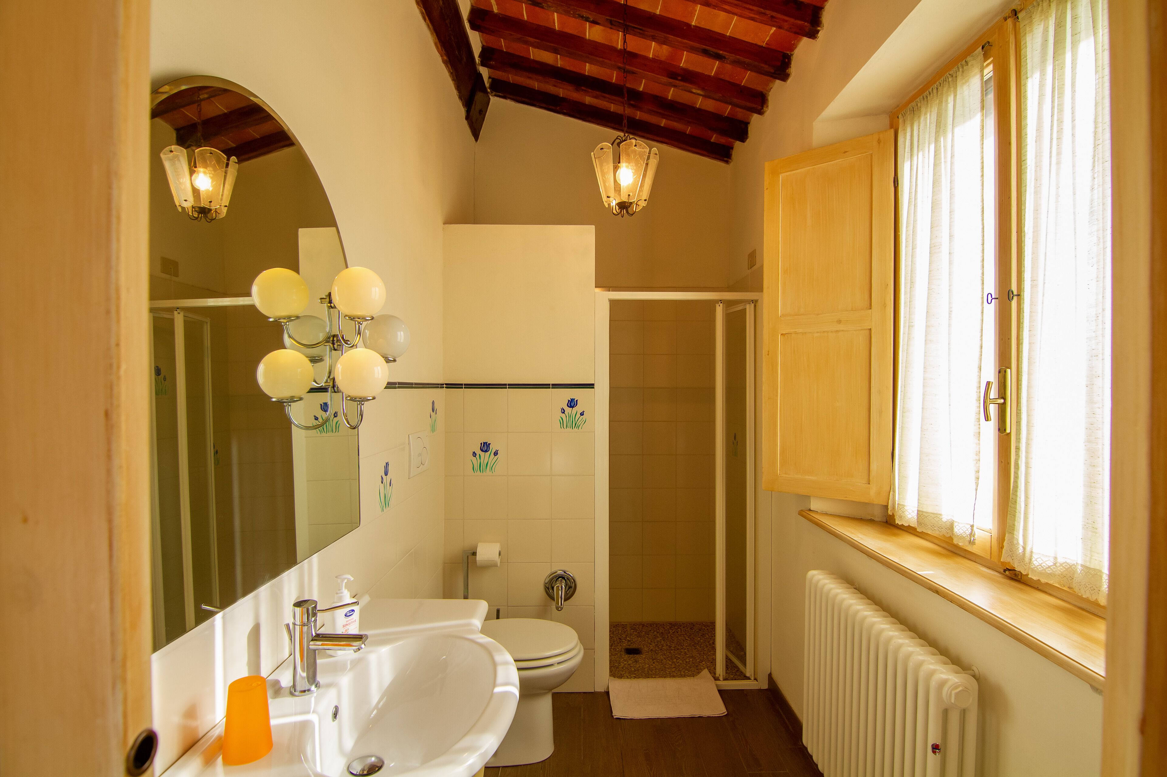 A bathroom with a sink, toilet, shower, and a window with curtains.