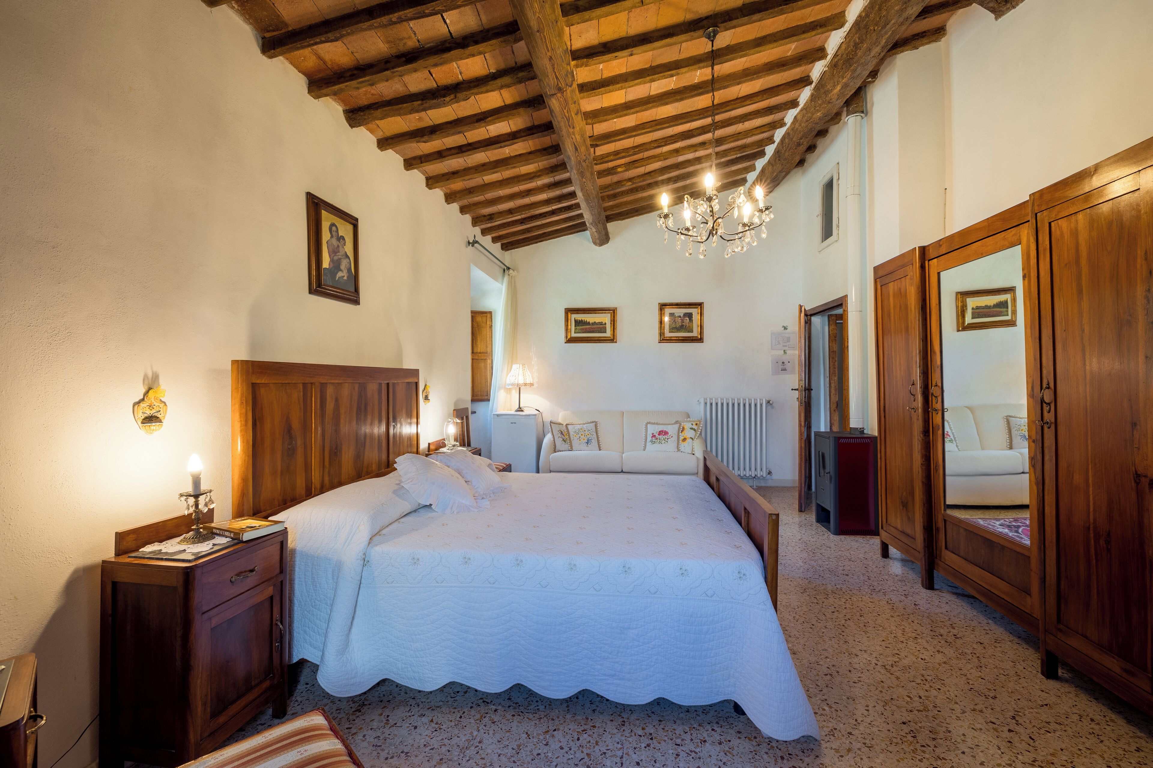 A bedroom with a wooden ceiling, a bed with a white bedspread, a nightstand with a lamp, and a dresser with a mirror.