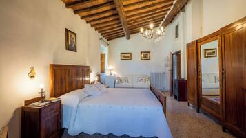 A bedroom with a wooden ceiling, a bed with a white bedspread, a nightstand with a lamp, and a dresser with a mirror.