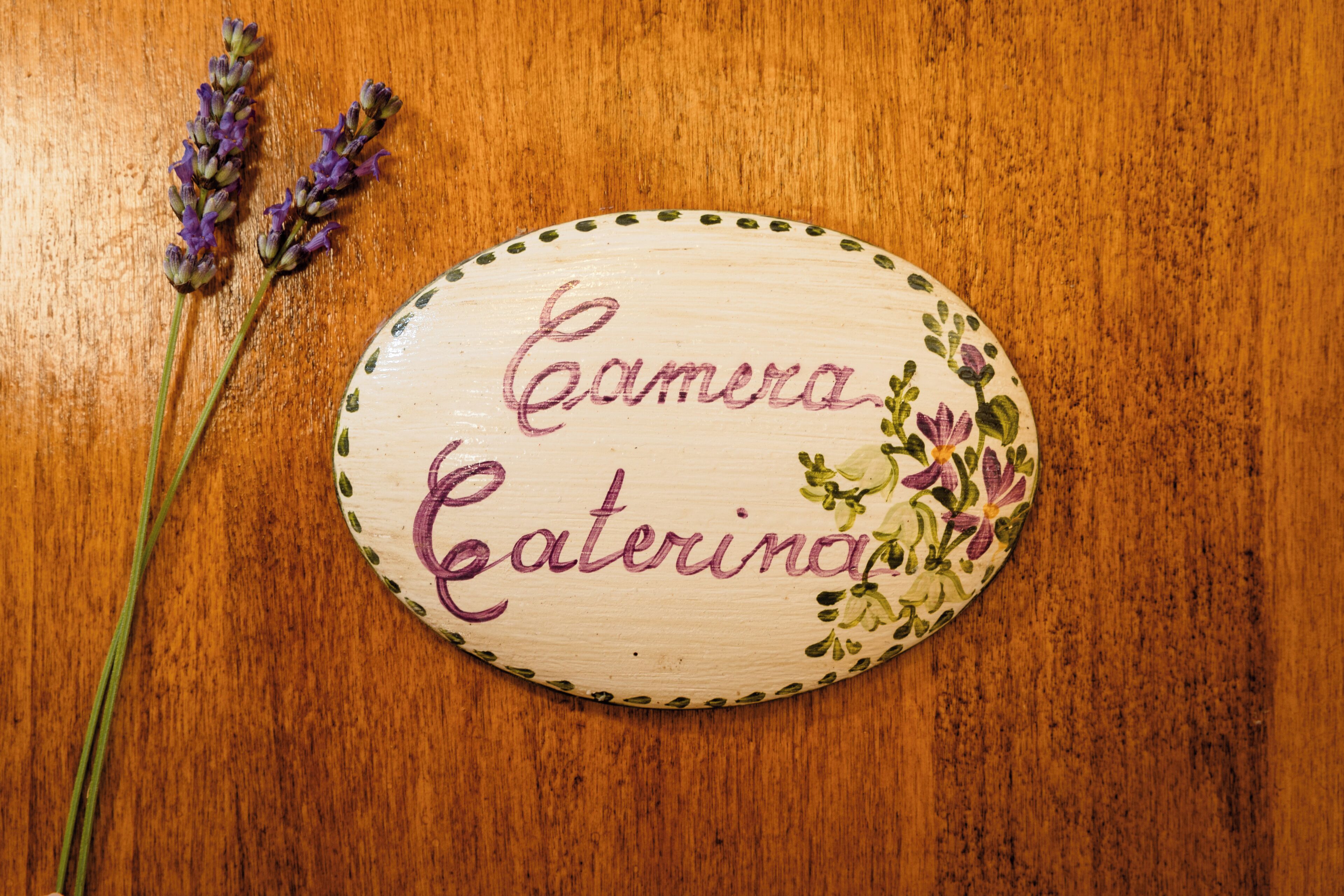 Eine hölzerne Plakette mit der Aufschrift "Camera Caterina" und einem Lavendelpflänzchen daneben.