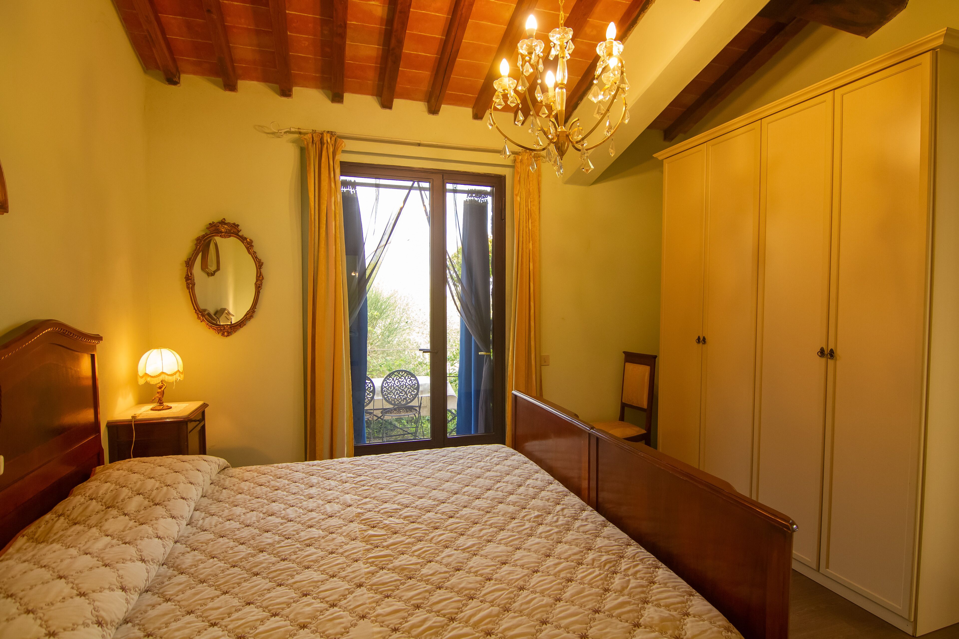 Een slaapkamer met een groot bed, een kroonluchter, een kledingkast en een raam met gordijnen.