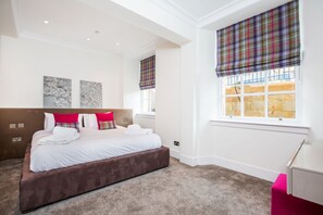Quarto com cama grande, duas janelas com cortinas xadrez, cabeceira e obra de arte na parede.