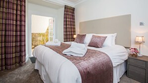 A hotel room with a large bed, a nightstand with a lamp, and a view of a stone building through the window. - Blythswood Square Apartments (Glasgow)