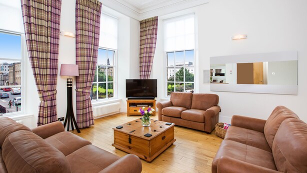 A modern living room with a large window, a flat-screen TV, and brown leather sofas. - Blythswood Square Apartments (Glasgow)