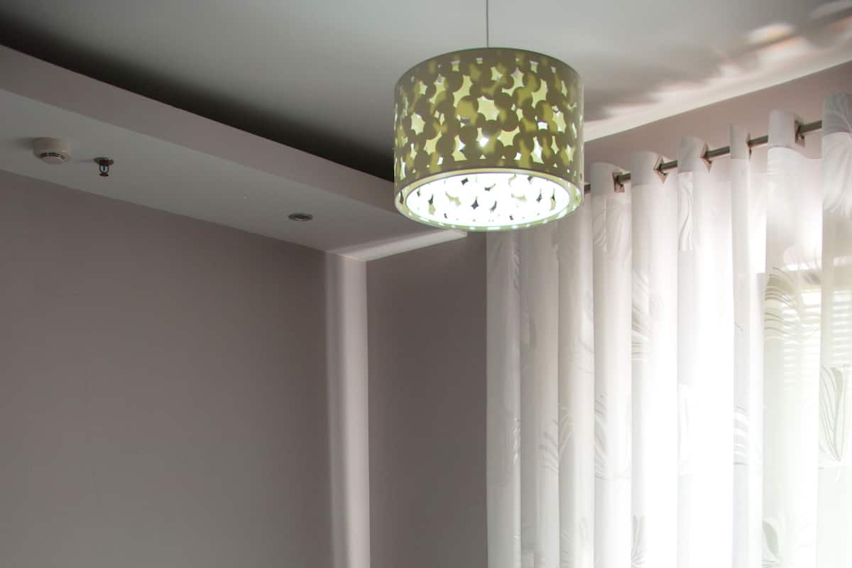 A neatly made bed with a quilted white duvet, a bedside table with a lamp, and sheer curtains.