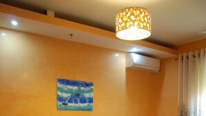 A bedroom with a wooden bed, a nightstand, a potted plant, a painting, and an air conditioning unit. - Hotel Gega (Berat)
