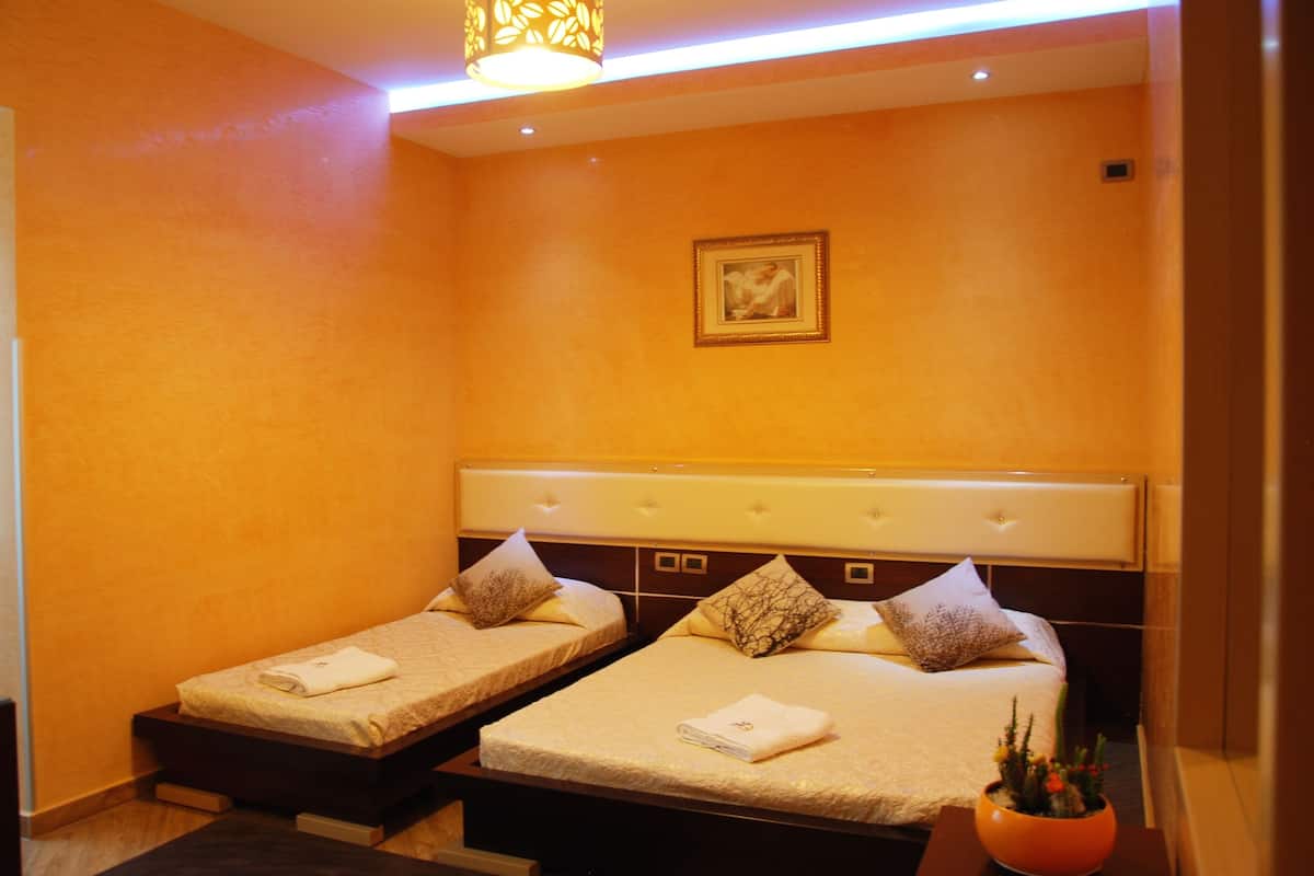A hotel room with two beds, a small table, and a wall-mounted picture.