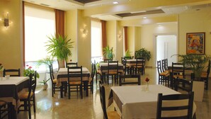 A dining area with multiple tables and chairs, potted plants, and a painting on the wall. - Hotel Gega (Berat)