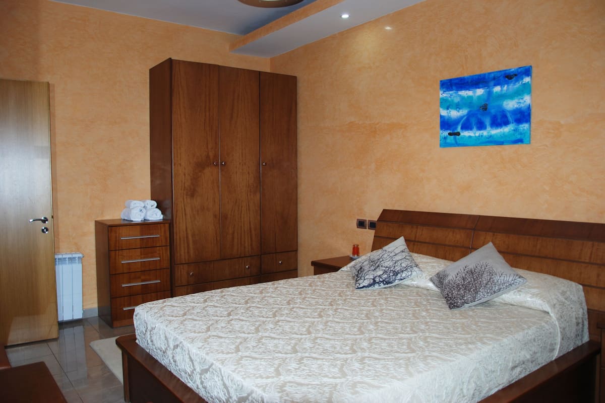 A bedroom with a large bed, wooden wardrobe, and a painting on the wall.