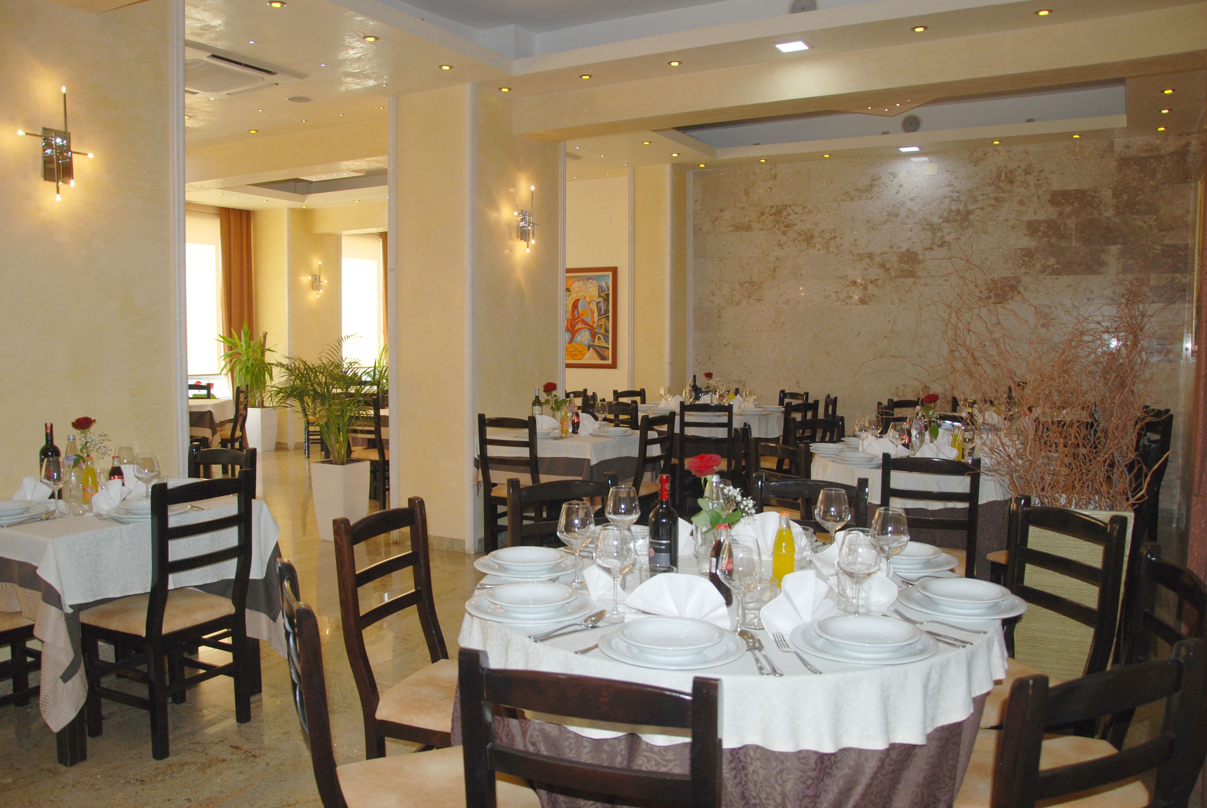 A restaurant with multiple round tables set for dining, each with white tablecloths, chairs, and dining utensils.