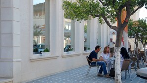 An outdoor cafe with tables and chairs, large windows, and a tree in the center. - Hotel Gega (Berat)