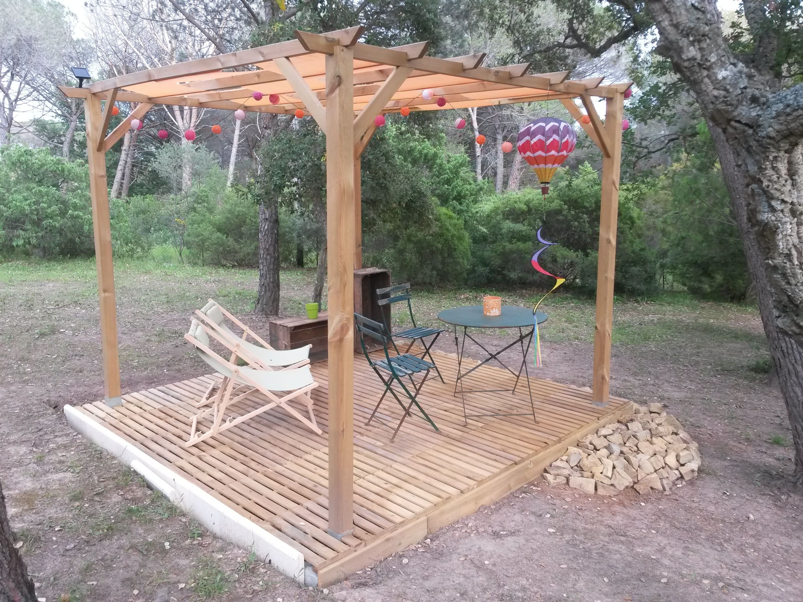 Une pergola en bois avec une table et des chaises, entourée d’arbres et décorée avec un ballon à air chaud.
