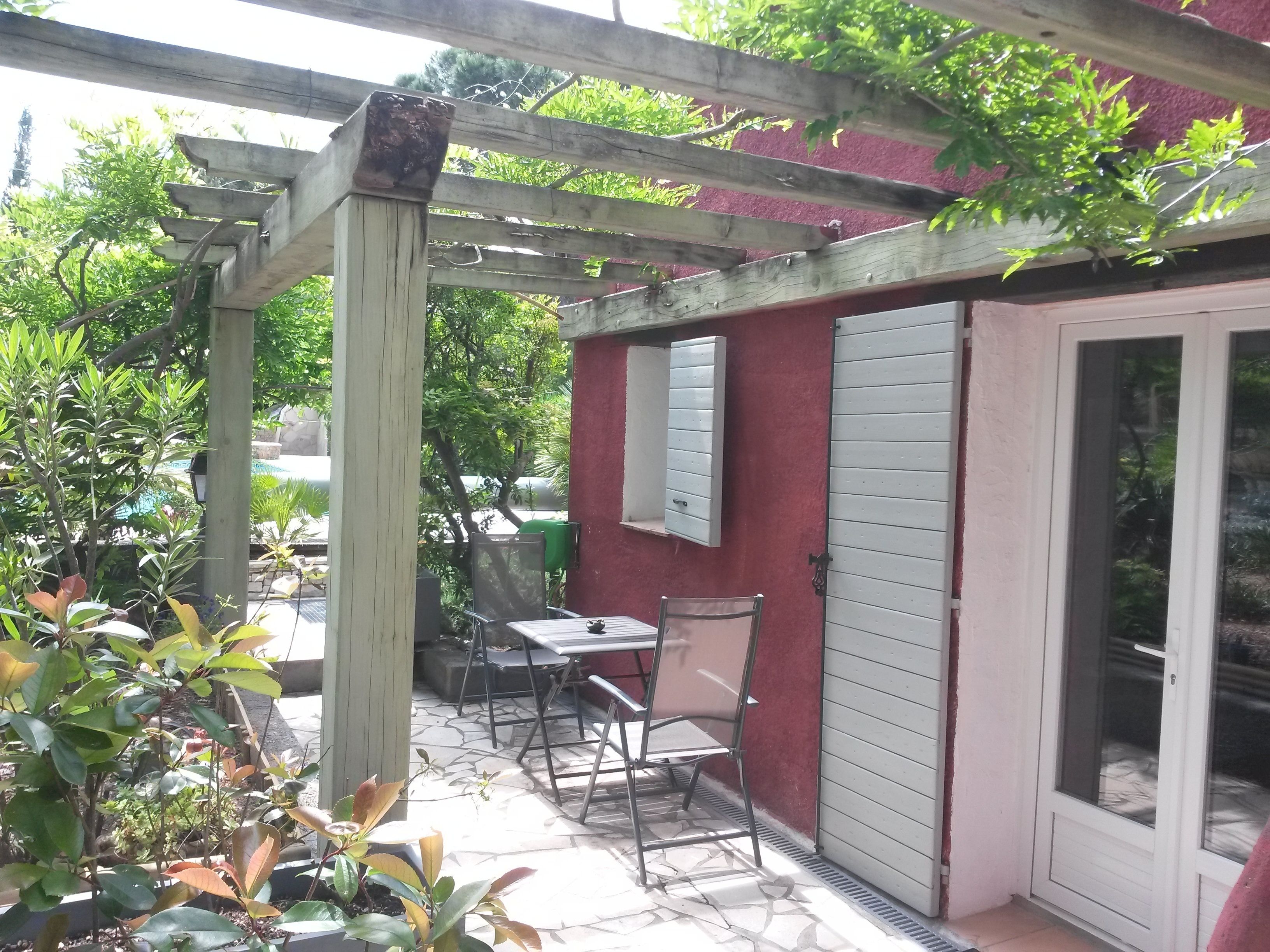 Un patio con una mesa, sillas, una pérgola y una puerta corrediza de vidrio.