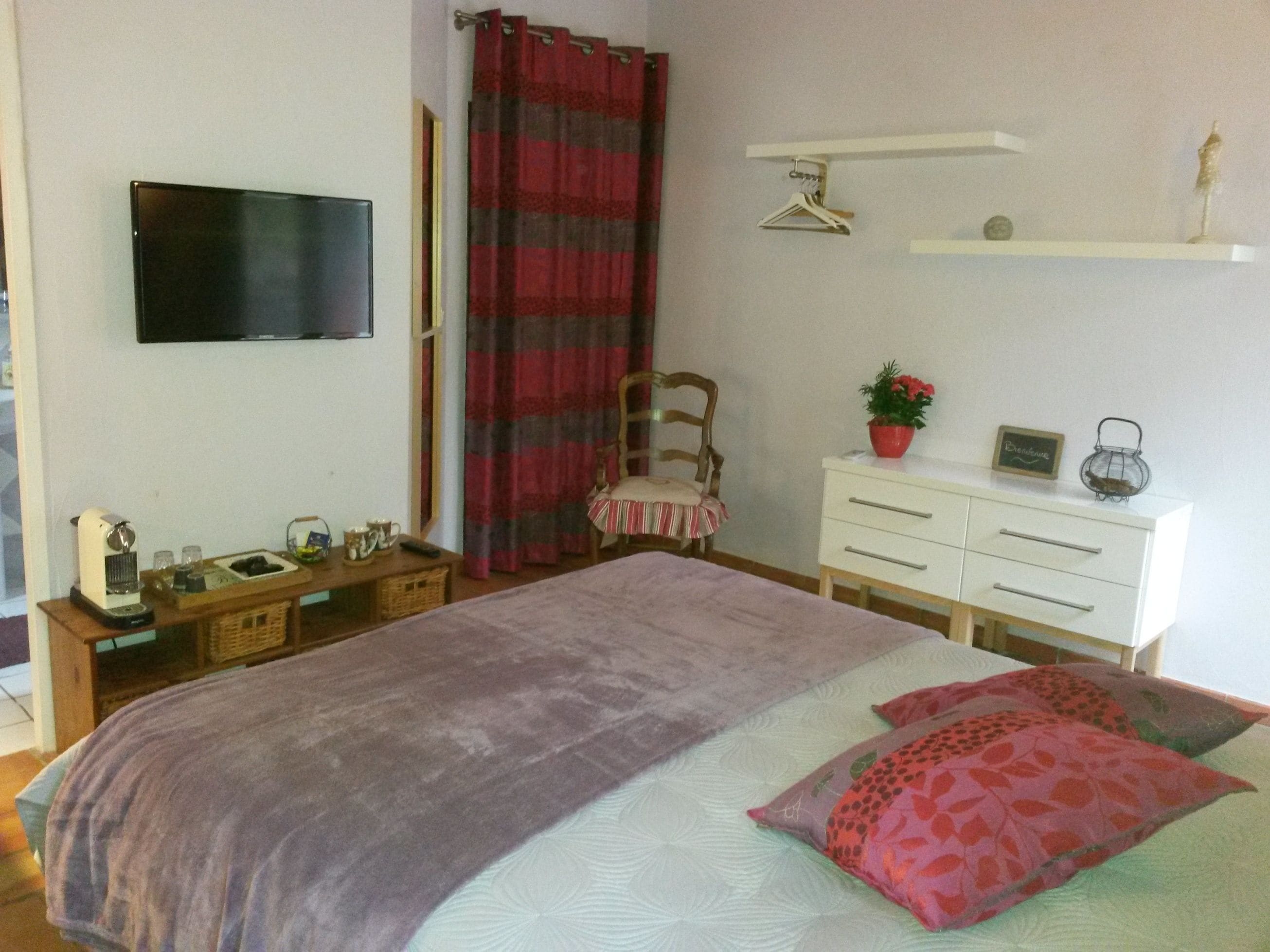 A bedroom with a bed, a dresser, a chair, a television, and a shelf with items.
