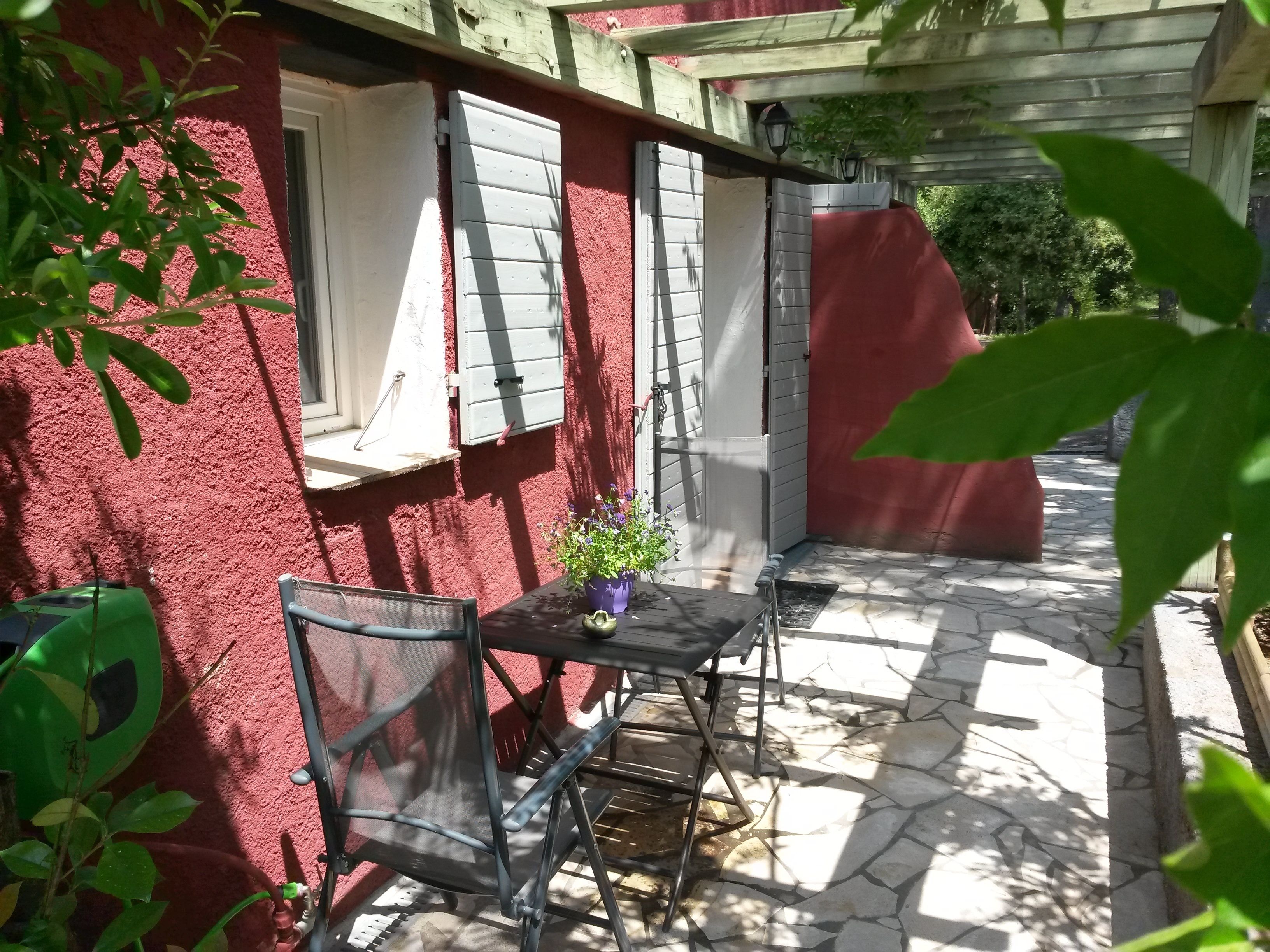 A patio with a table and chairs, a potted plant, and a red wall.