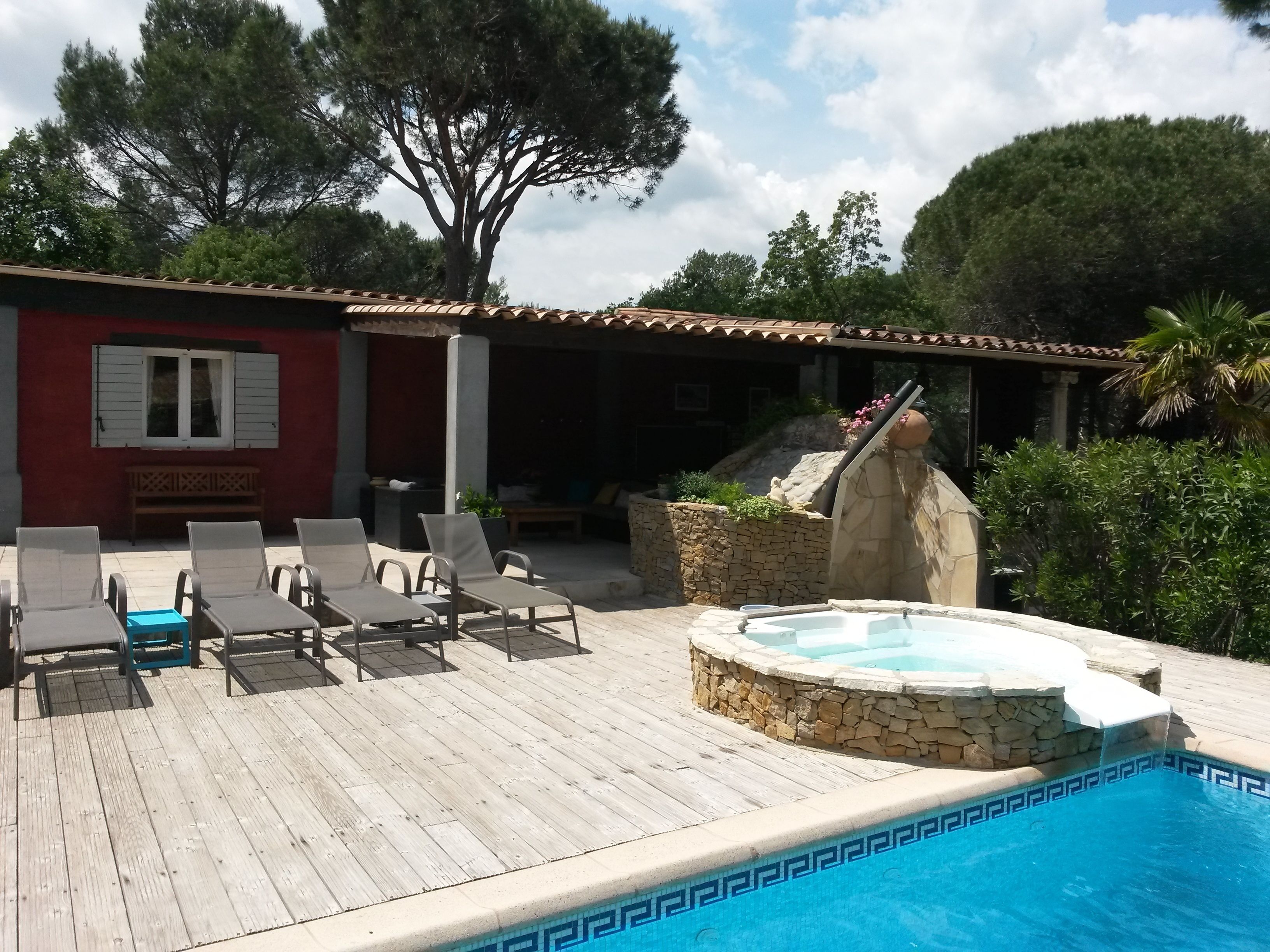 A wooden deck with lounge chairs, a stone hot tub, and a pool with a decorative edge.