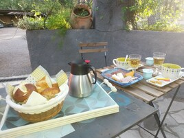 Desayuno con pan, queso, jamón y una cafetera sobre una mesa al aire libre.