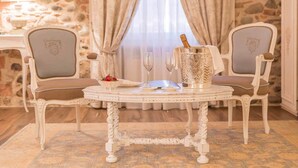 A room with a stone wall, two upholstered chairs, a round table with a bottle of champagne, two glasses, and a bowl of fruit. - Maison Resola (Valeggio sul Mincio)