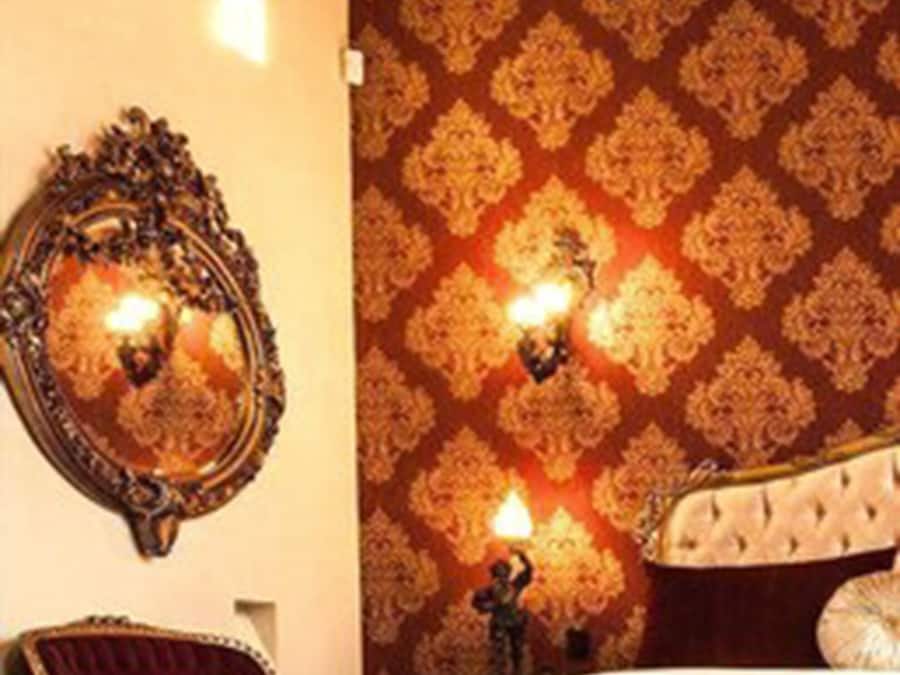 A bedroom with a large bed, ornate wall sconces, a mirror, and a red chair.