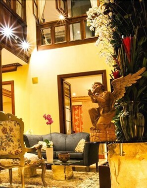 A living room with a sofa, a chair, a coffee table, and a statue of an angel. - The Orchids Hotel (Bogotá)