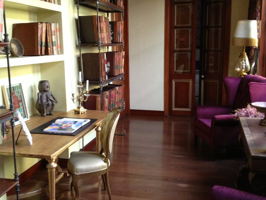 A library with wooden bookshelves, a reading table, and a purple armchair.