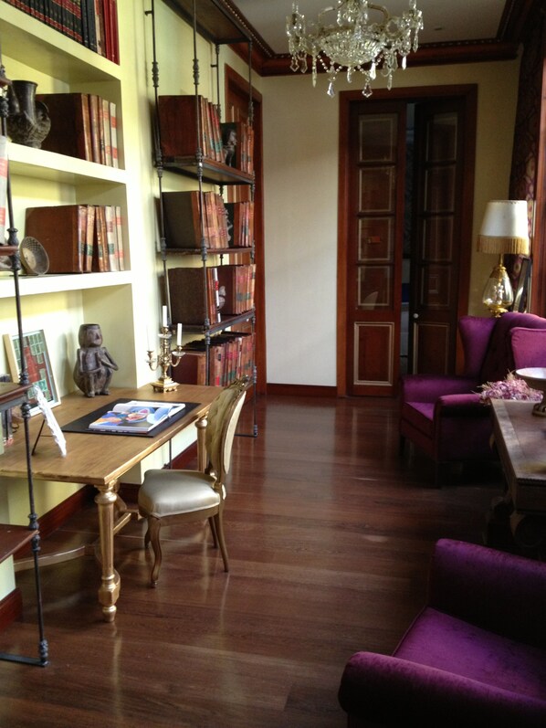 A library with wooden bookshelves, a reading table, and a purple armchair. - The Orchids Hotel (Bogotá)