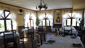 A restaurant with multiple tables set for dining, featuring a chandelier, large windows with curtains, and a tiled floor. - Rincón de Pepe (El Castell de Guadalest)