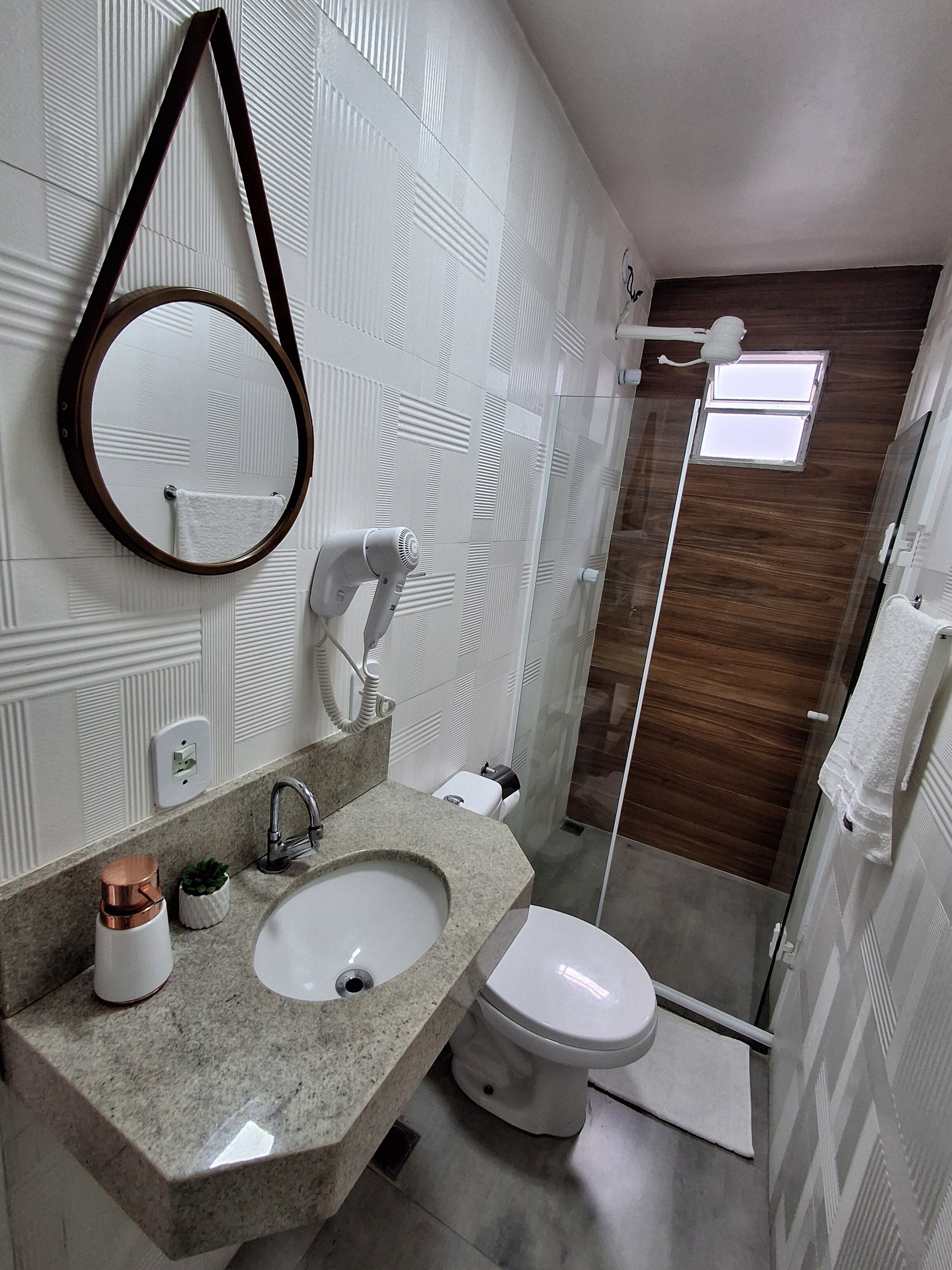 A modern bathroom with a granite countertop, a white sink, a toilet, and a shower area.