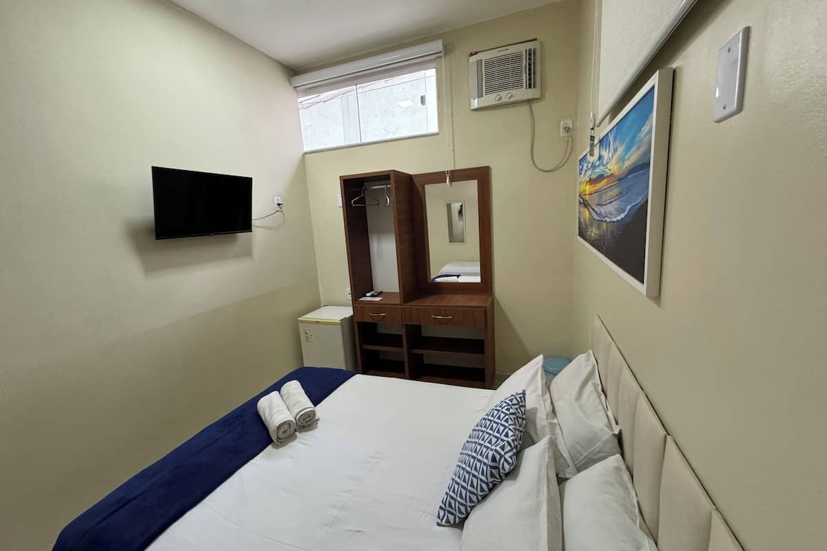 Habitación de hotel con cama, televisión montada en la pared, armario, escritorio pequeño y un cuadro.