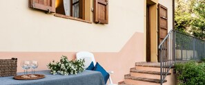 A table set with glasses and flowers, a wicker bag, and a chair outside a building with wooden shutters and a metal railing. - Tenuta degli Obizzi (Montecarlo)