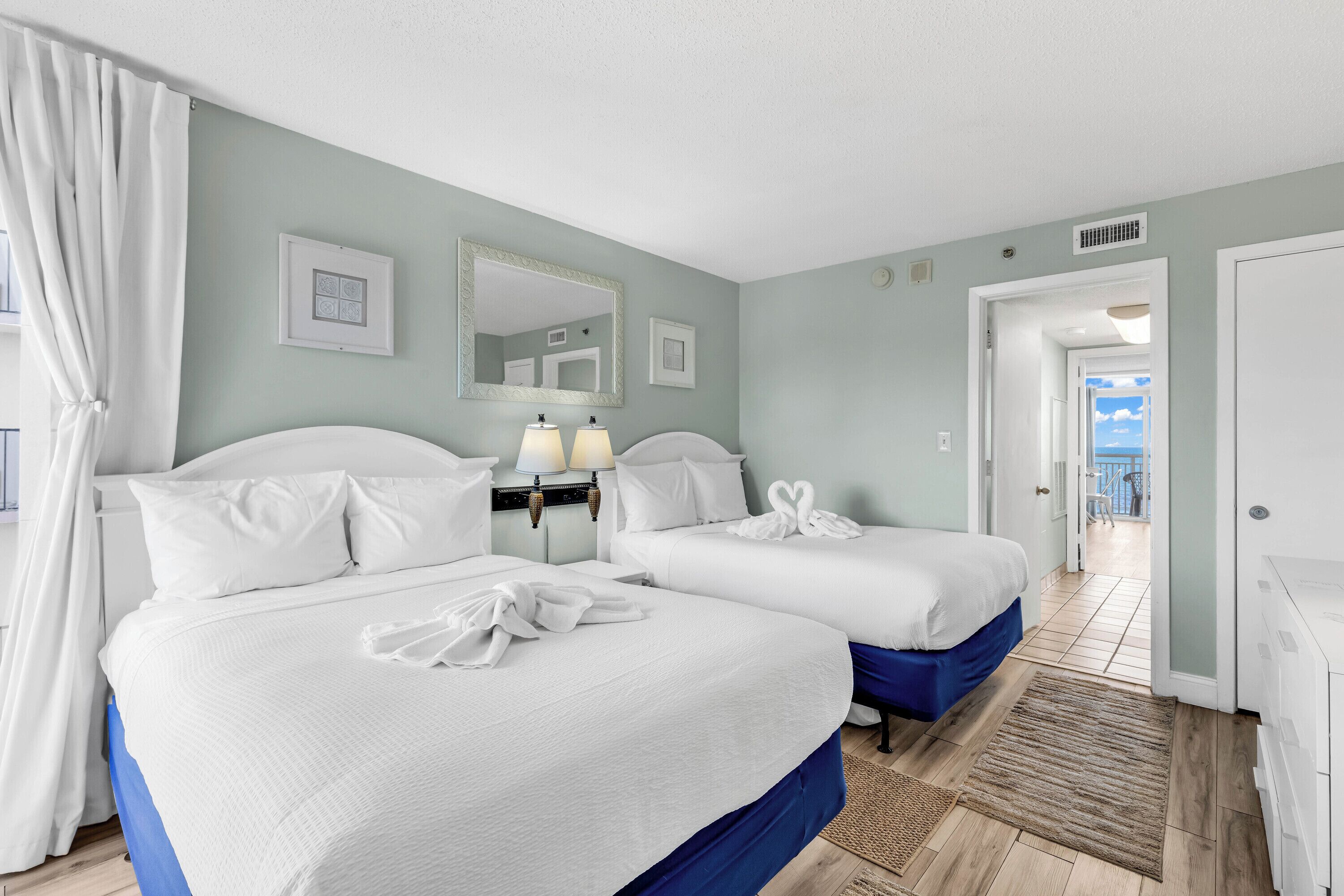 A hotel room with two beds, a bathroom with a shower, and a view of the sea.