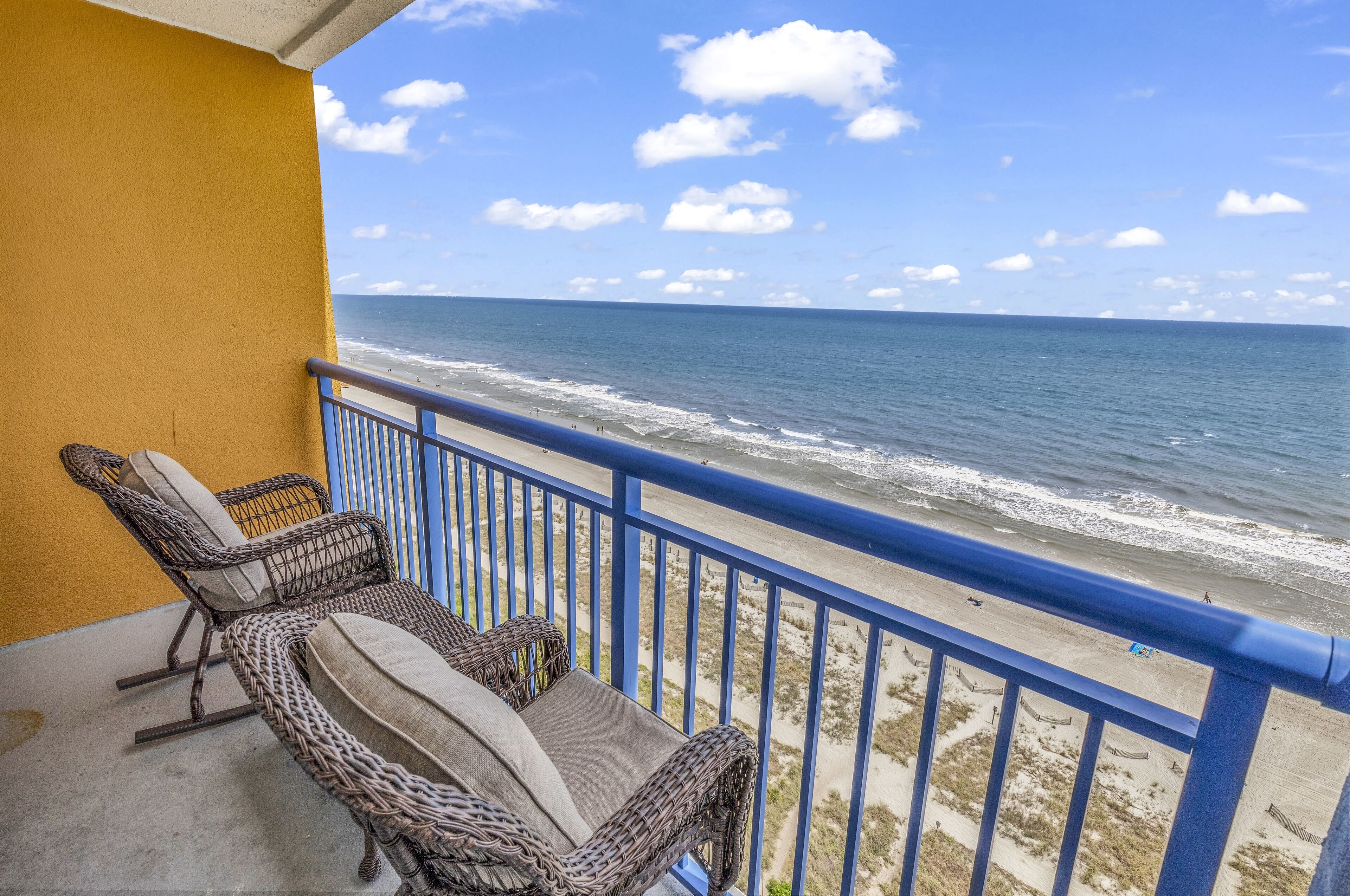 A balcony with wicker furniture overlooking a beach.
