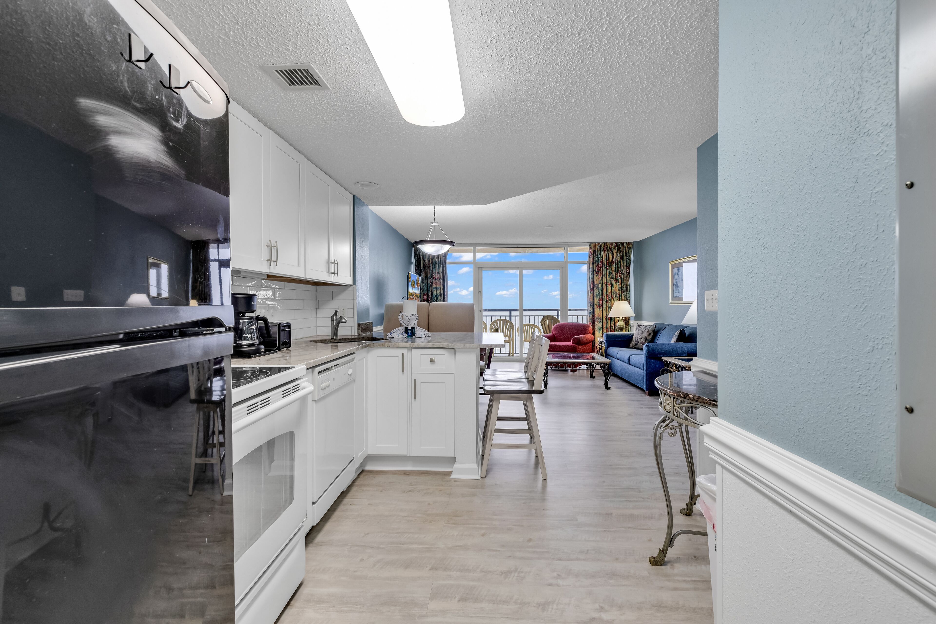 A modern kitchen with white cabinets, a large island, and a dining area with a red chair and a blue sofa.