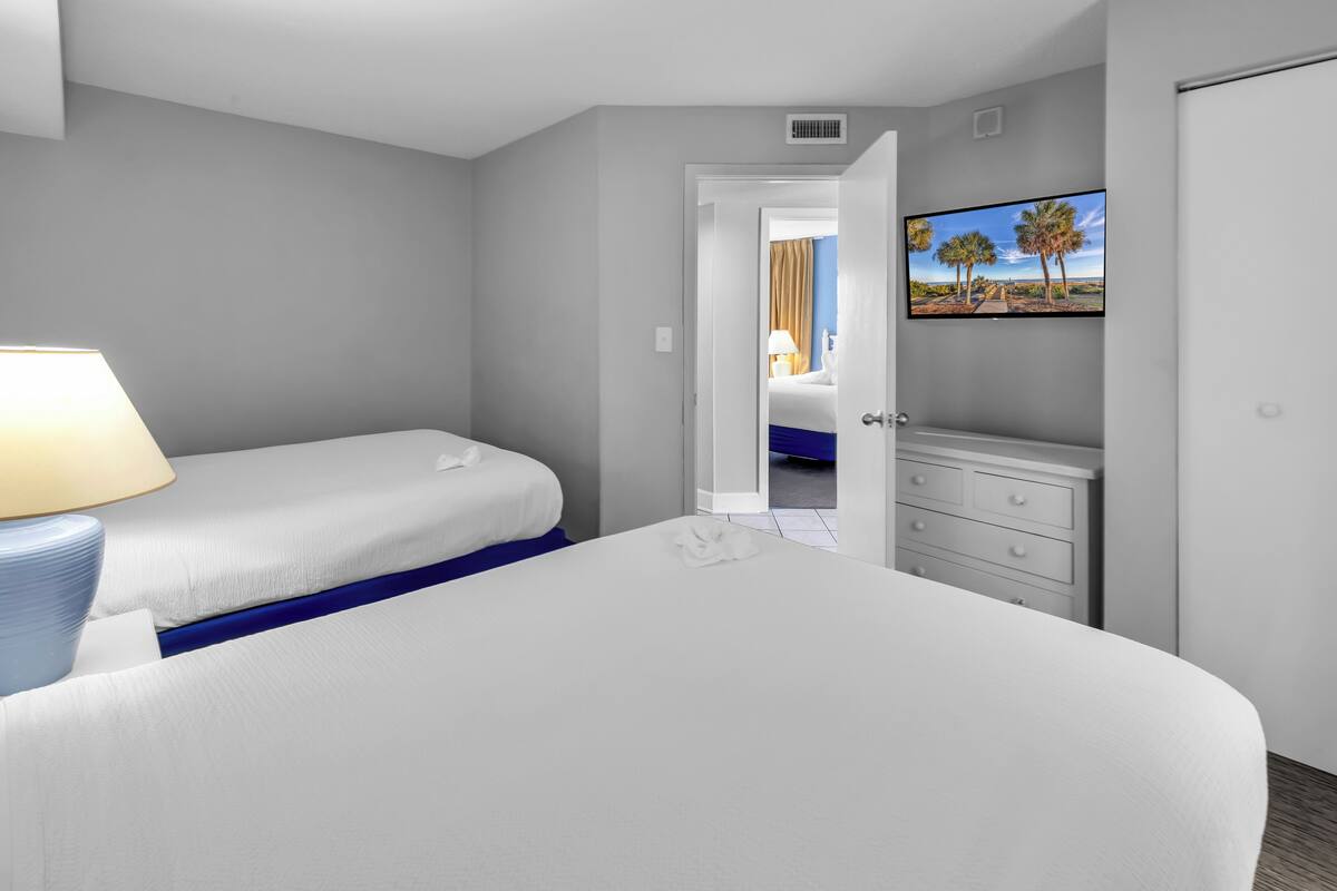 A hotel room with a bed, a desk, a chair, a lamp, a TV, and a wardrobe.