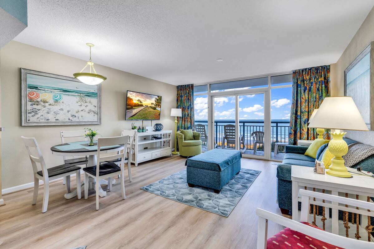 A spacious living room with a dining area, a sofa set, and a balcony with a view.