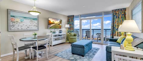 A spacious living room with a dining area, a sofa set, and a balcony with a view.