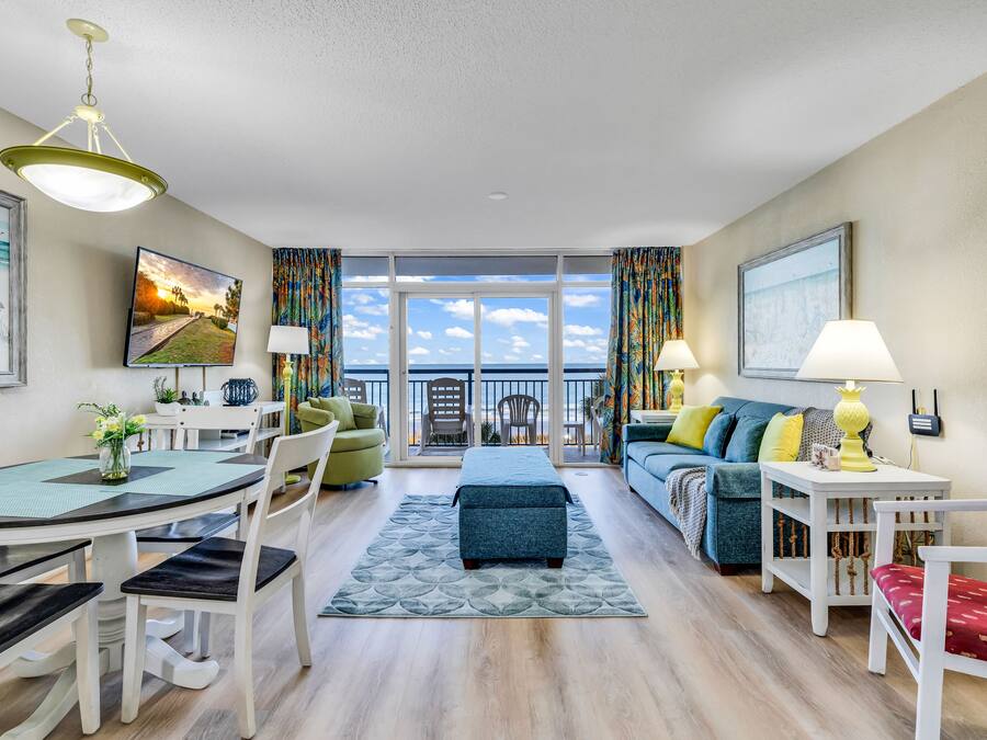 Uma sala de estar moderna com área de jantar, sofás e vista para o mar.