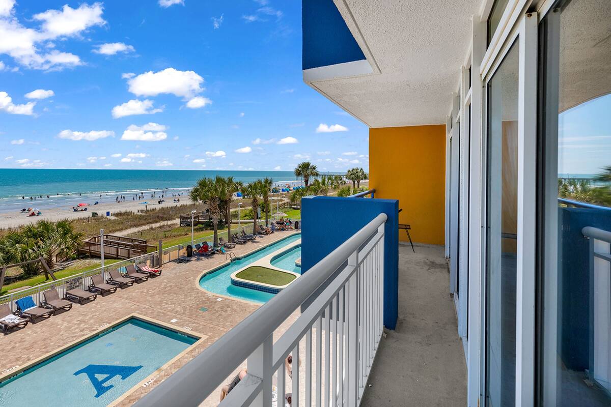 A balcony with a view of a beach and a pool area.