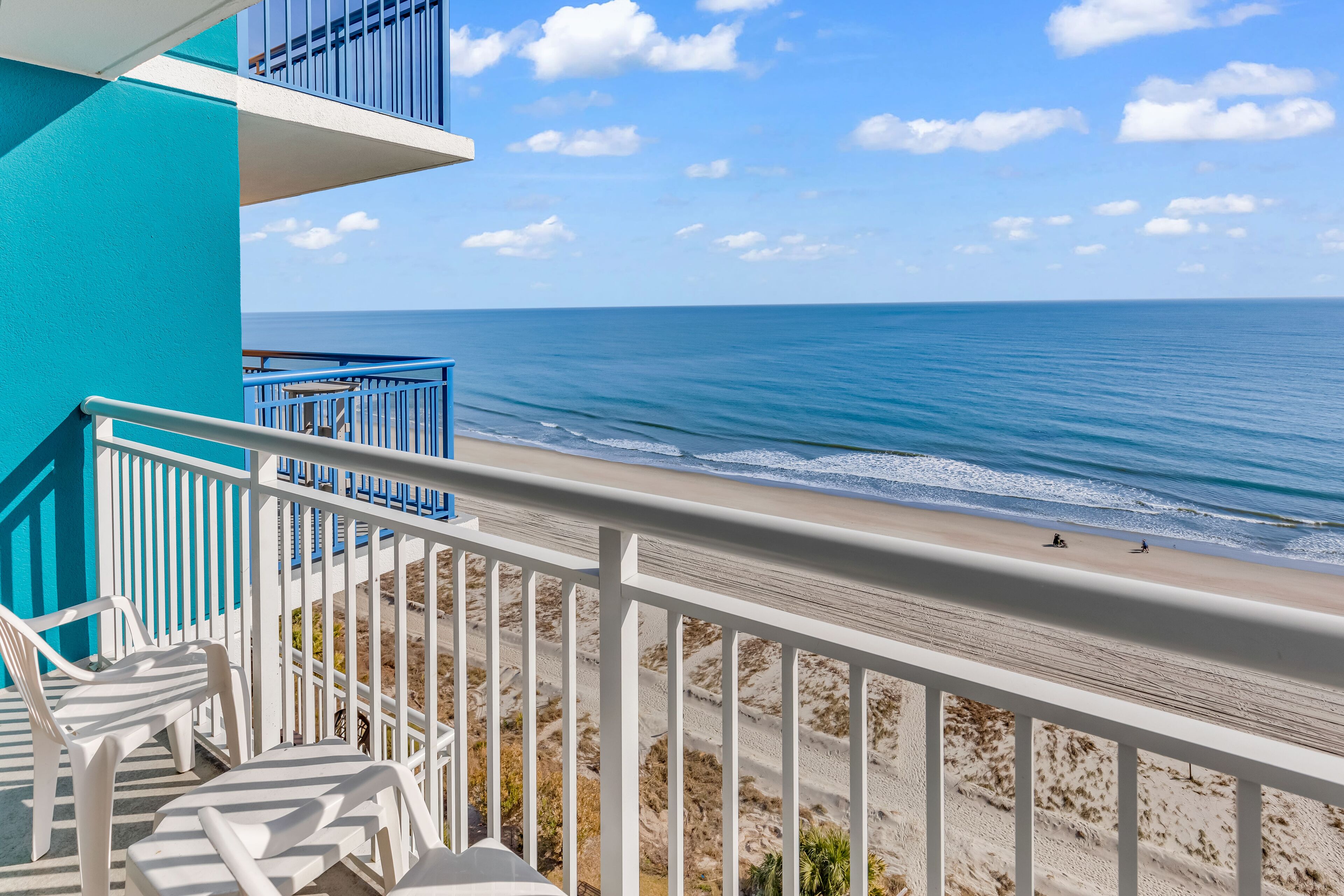 A balcony with white railings overlooking a beach with a clear view of the ocean.