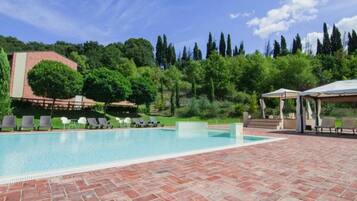 A swimming pool with lounge chairs, a gazebo, and a brick patio.
