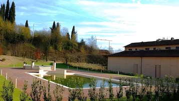 A landscaped area with a pool, a building with a flat roof, and trees in the background.