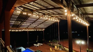 Uma área externa coberta com piscina, cadeiras de descanso e luzes pendentes.